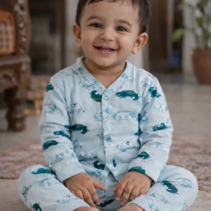 Smiling baby wearing crocodile print cotton co-ord set sitting indoors in natural light.